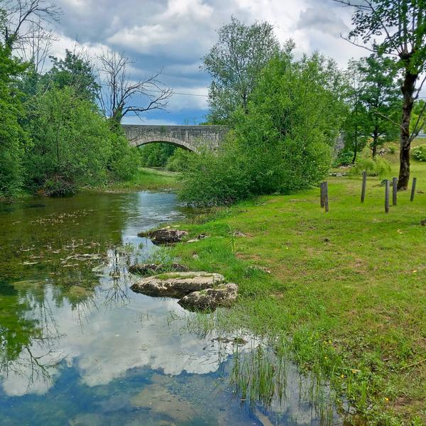 Plitki tok rijeke s kamenjem i mostom u pozadini